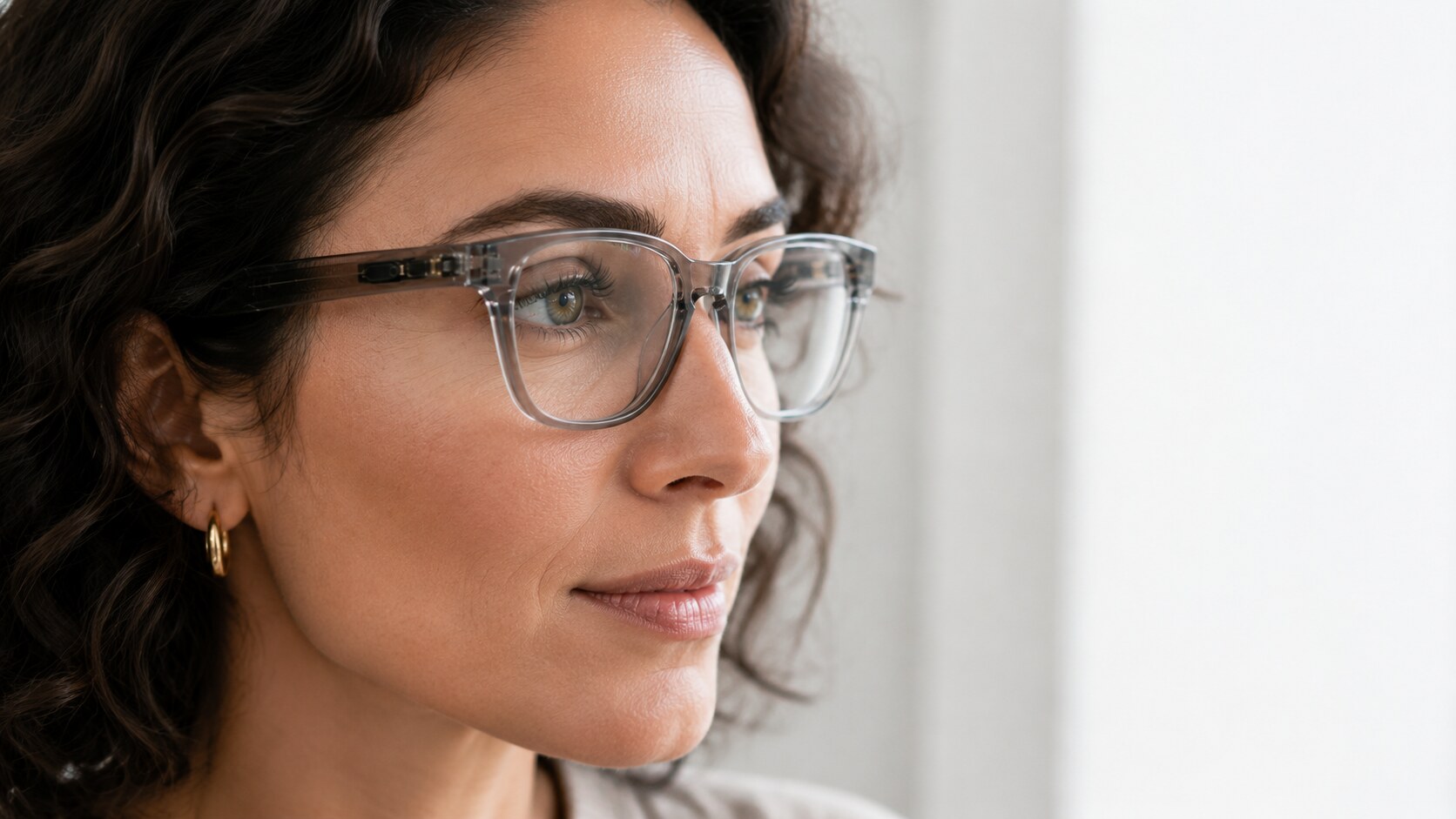 Woman wearing clear-framed Motia glasses, looking into the distance, with the sensor visible in the temple